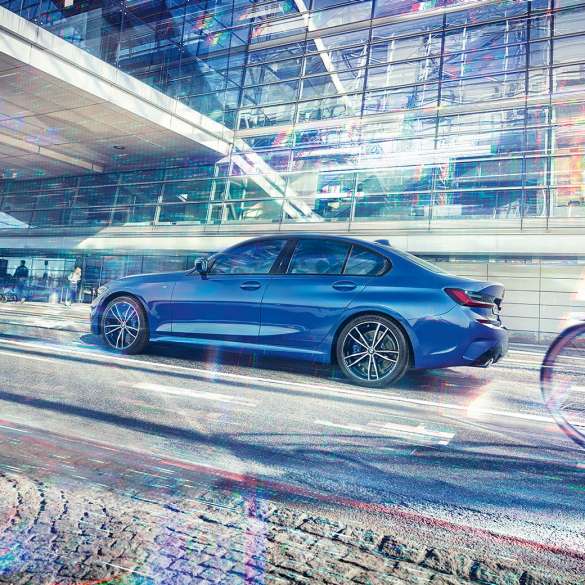 BMW 3er Limousine, Seitenansicht G20. Seitliche Standaufnahme der BMW 3er Limousine am Tag vor gläsernem Gebäude G20.