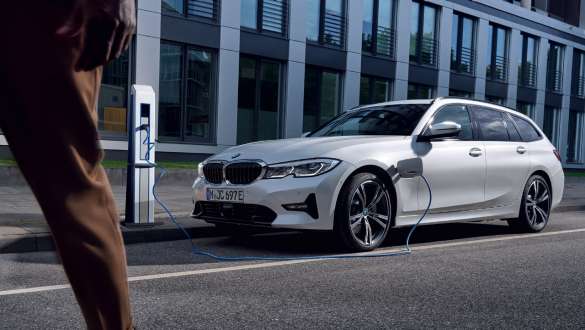 Plug-in-Hybrid BMW 3er Touring 2021 G21 Dreiviertel-Frontansicht ladend Plug-in-Hybrid BMW 3er Touring 2021 G21 Dreiviertel-Frontansicht ladend vor Gebäude