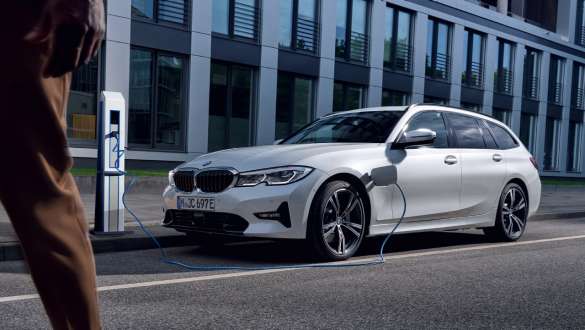 Plug-in-Hybrid BMW 3er Touring 2021 G21 Dreiviertel-Frontansicht ladend Plug-in-Hybrid BMW 3er Touring 2021 G21 Dreiviertel-Frontansicht ladend vor Gebäude