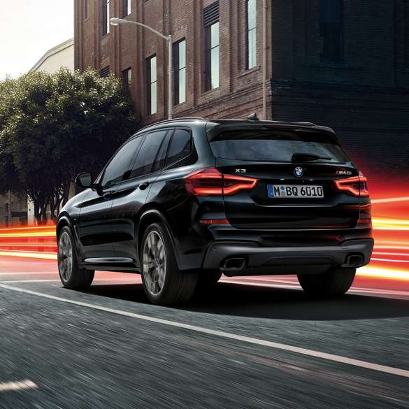 BMW X3 M40i SUV, Dreiviertel-Heckansicht G01. BMW X3 M40i SUV in Saphierschwarz metallic, fahrend, Exterieur, Dreiviertel-Heckansicht vor städtischer Kulisse mit Lichtstreifen G01.