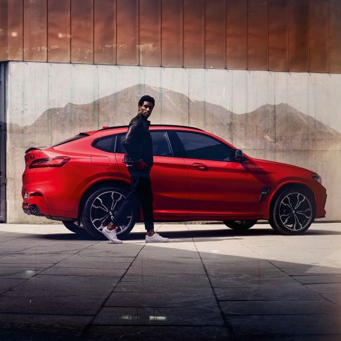 BMW X4 M Competition, Seitenansicht mit jungem Mann. BMW X4 M Competition in Toronto Rot metallic, Exterieur, Seitenansicht mit jungem Mann.