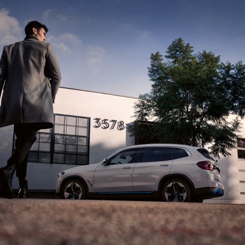 BMW iX3 G08 Seitenansicht vor Gebäude mit Mann BMW iX3 G08 2020 Mineralweiß metallic Seitenansicht vor Gebäude mit Mann