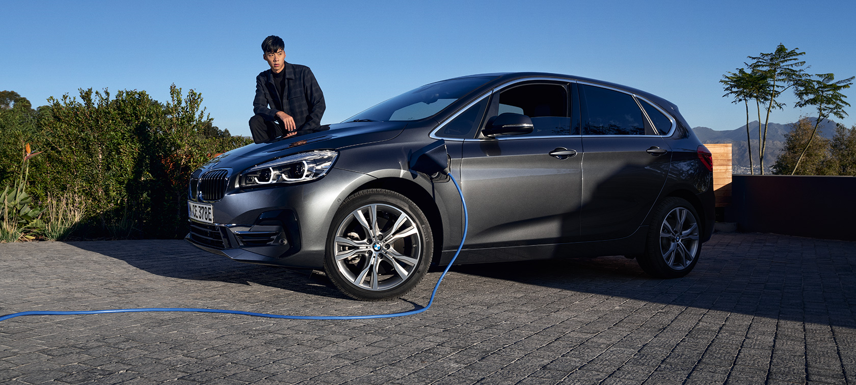BMW 225xe Active Tourer F45 hybride rechargeable, vue de trois quarts de profil, branchée à une borne BMW 225xe Active Tourer F45 hybride rechargeable, vue de trois quarts de profil, branchée à une borne avec modèle