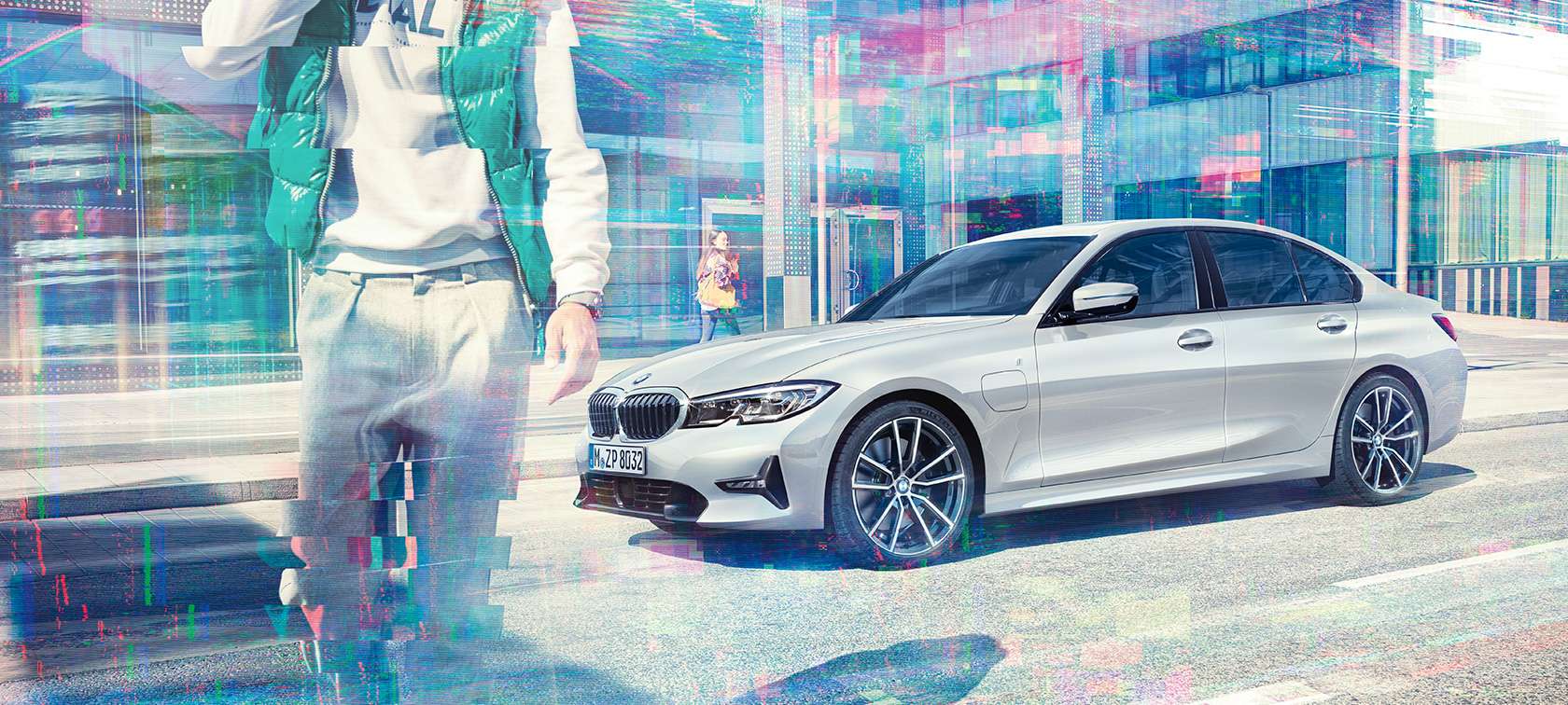 BMW 3er Limousine, Seitschuss BMW 330e. G20 Dreiviertel-Seitschuss der stehenden BMW 330e Limousine vor urbanem Glasgebäude mit sich bewegenden Passanten. G20