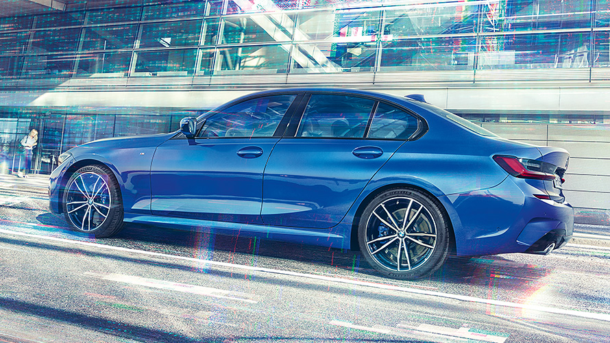 BMW Série 3 Berline (G20) de jour devant des immeubles en verre Vue de profil de la BMW Série 3 Berline (G20) Portimao Blau au repos, de jour devant des immeubles en verre.