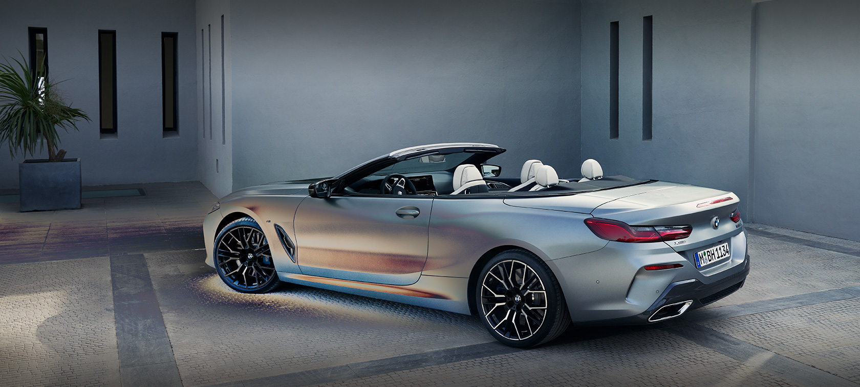 Homme appuyé sur une BMW Série 8 Cabrio G14 LCI restylage 2022 BMW Individual BMW Individual Frozen Pure Grey metallic, vue de profil, devant un bâtiment