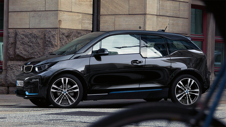 BMW i3s I01 2018 en Fluid Black avec accent BMW i Blau vue de profil en mouvement dans un décor urbain