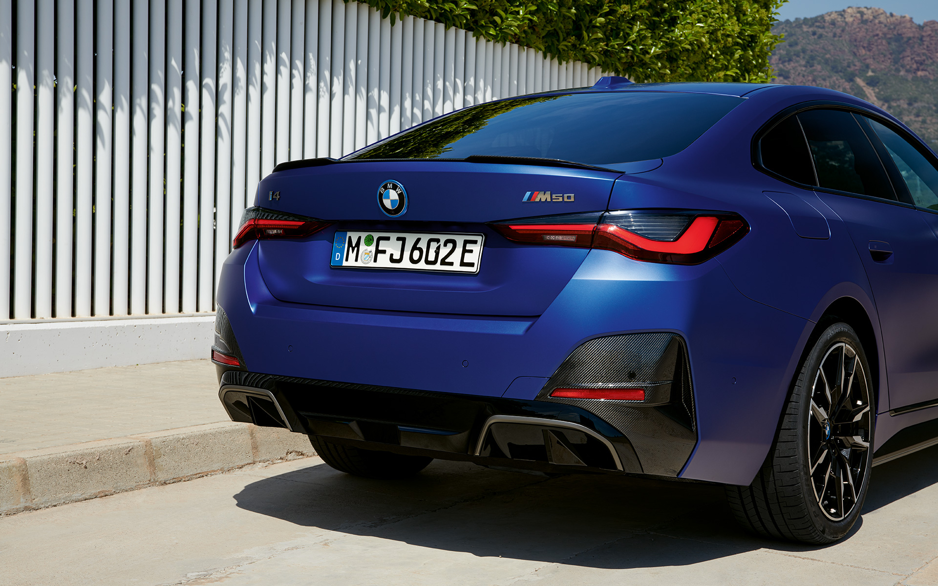 BMW i4 M50 G26 2021 BMW Individual Frozen Portimao Blau metallic Dreiviertel-Heckansicht stehend am weißen Zaun