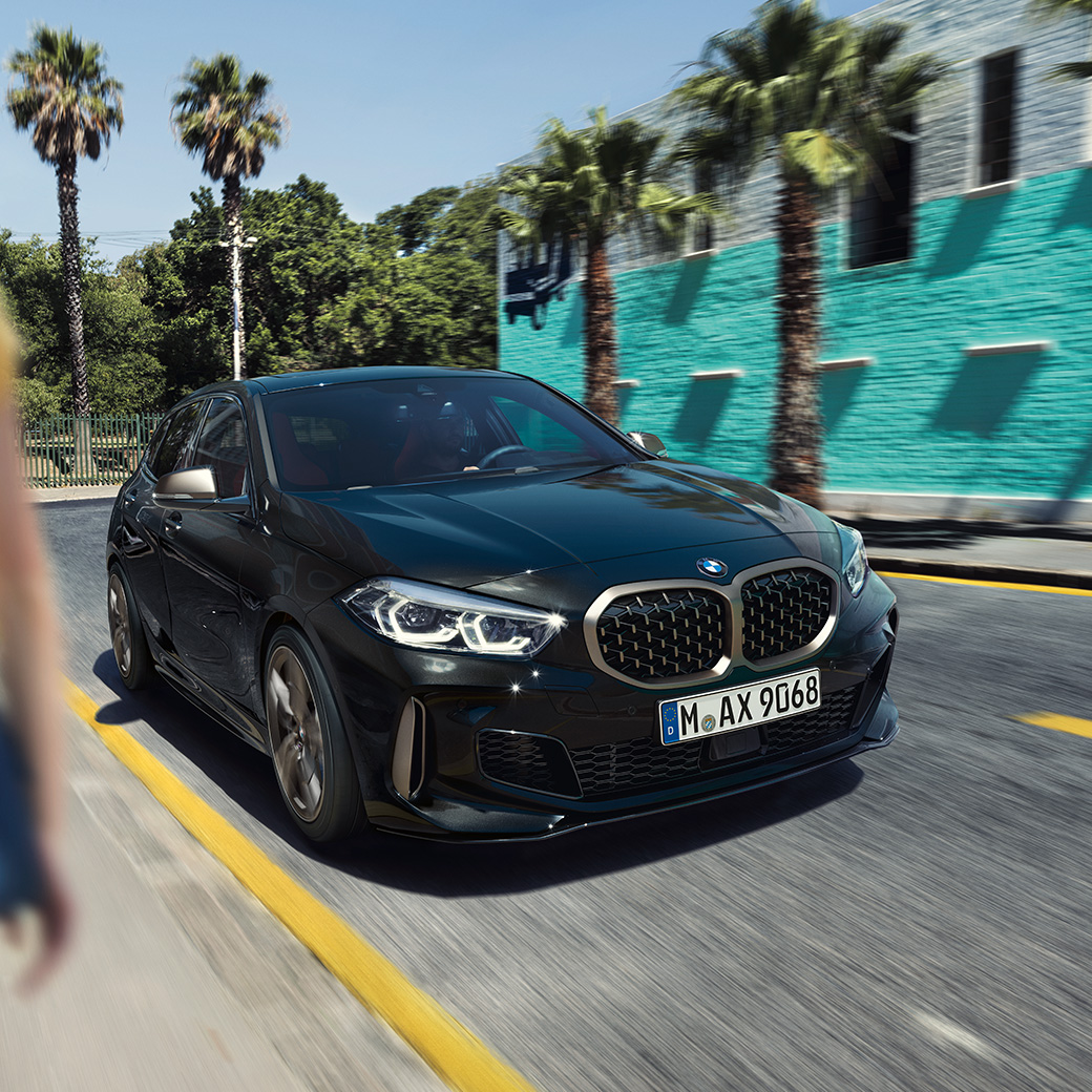 BMW M135i xDrive, Dreiviertel-Frontansicht F40. BMW M135i xDrive in Saphirschwarz metallic, Dreiviertel-Frontansicht fahrend mit Frau im Vordergrund F40.
