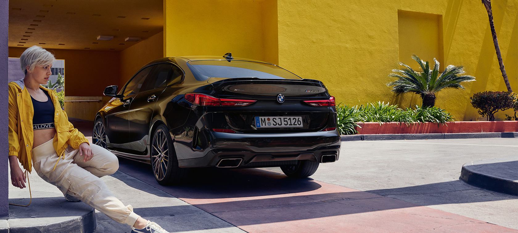 BMW M235i xDrive Gran Coupé Dreiviertel-Heckansicht F44 BMW M235i xDrive Gran Coupé Saphirschwarz metallic F44 Dreiviertel-Heckansicht mit Frau im Vordergrund
