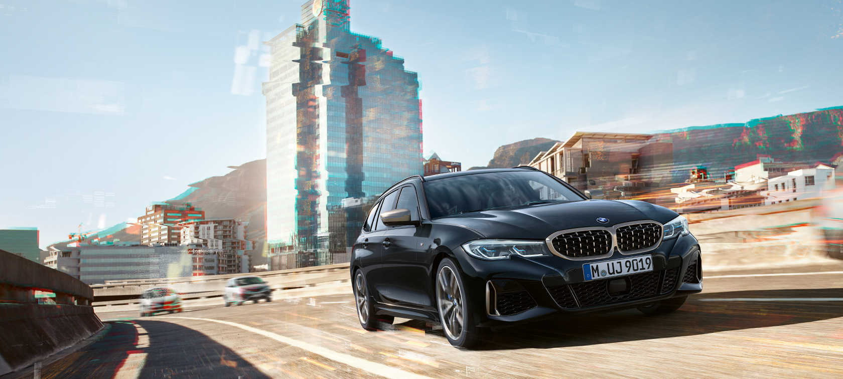 Dreiviertel-Frontaufnahme im fahren vor urbaner Kulisse BMW M340i xDrive Touring, Dreiviertel-Frontaufnahme im fahren vor urbaner Kulisse