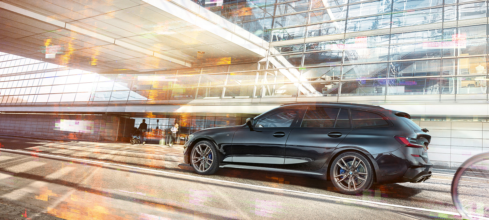 BMW M340i xDrive Touring, seitliche Fahraufnahme G21 BMW M340i xDrive Touring, seitliche Fahraufnahme vor urbanem Glasgebäude G21