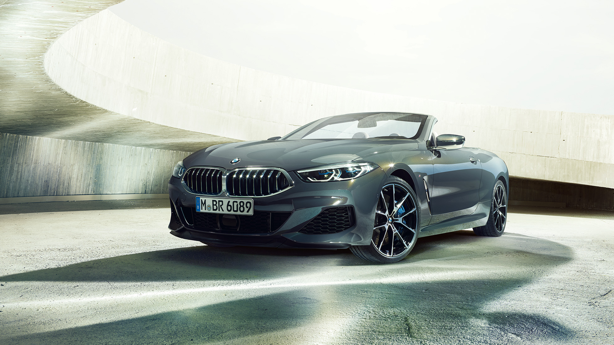 BMW M850i xDrive Cabriolet, Dreiviertel-Frontansicht. BMW M850i xDrive Cabriolet in Dravitgrau metallic mit geöffnetem Verdeck, Dreiviertel-Frontansicht, stehend in Betongebäude.