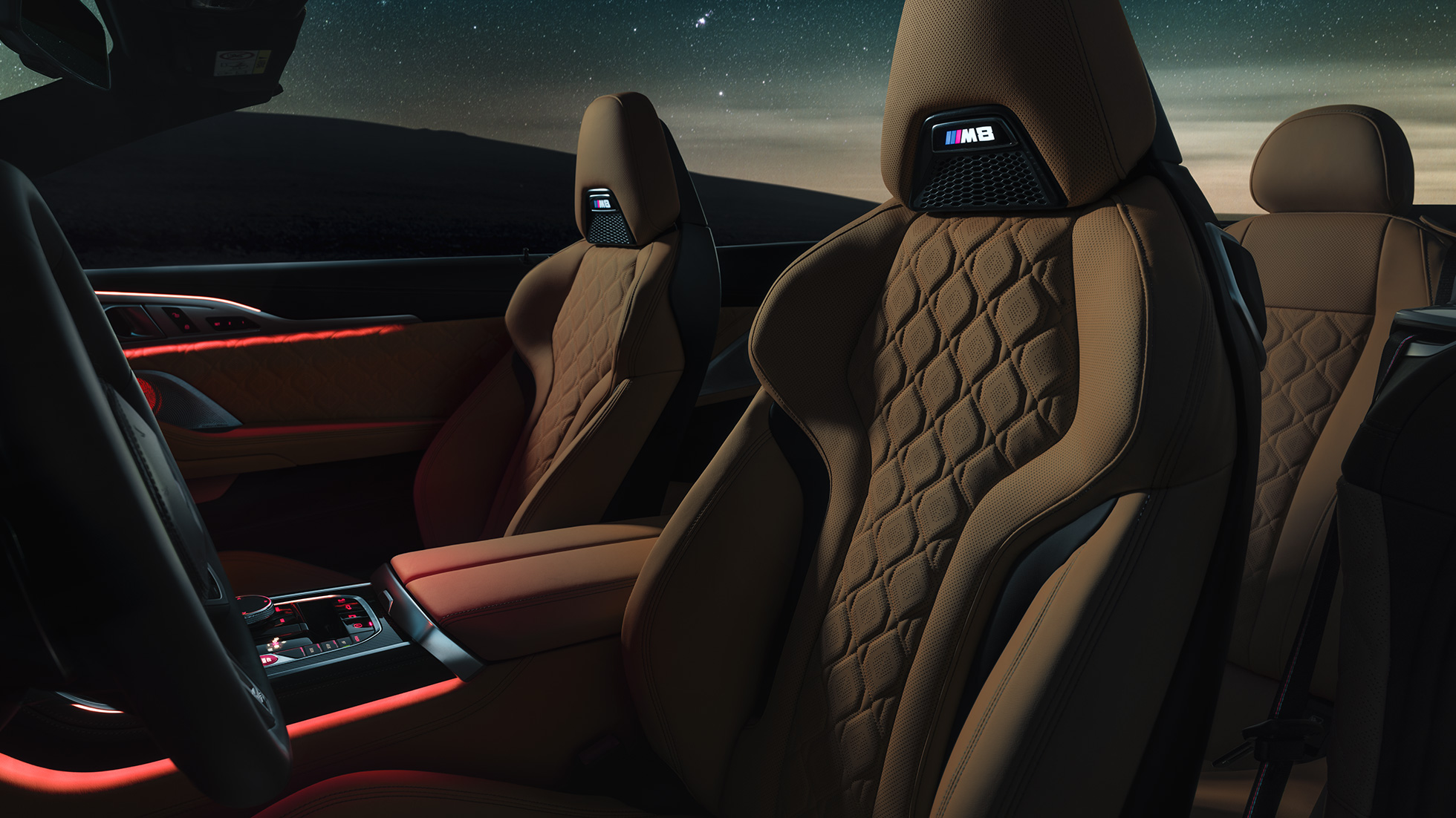 M Sportsitze in Leder 'Merino'. BMW M8 Competition Cabriolet mit geöffnetem Verdeck unter Sternenhimmel, Innenraum mit M Sportsitzen in Leder 'Merino' und rotem ambienten Licht.