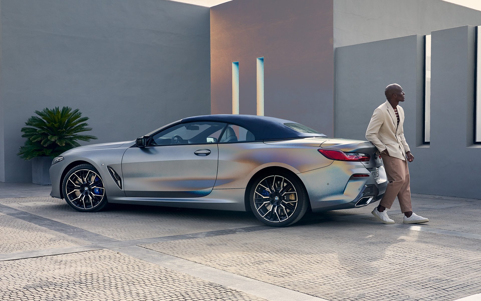 BMW M850i xDrive Cabrio G14 LCI Facelift 2022 BMW Individual Frozen Pure Grey metallic Dreiviertel-Heckansicht mit männlichem Model an das Fahrzeug gelehnt