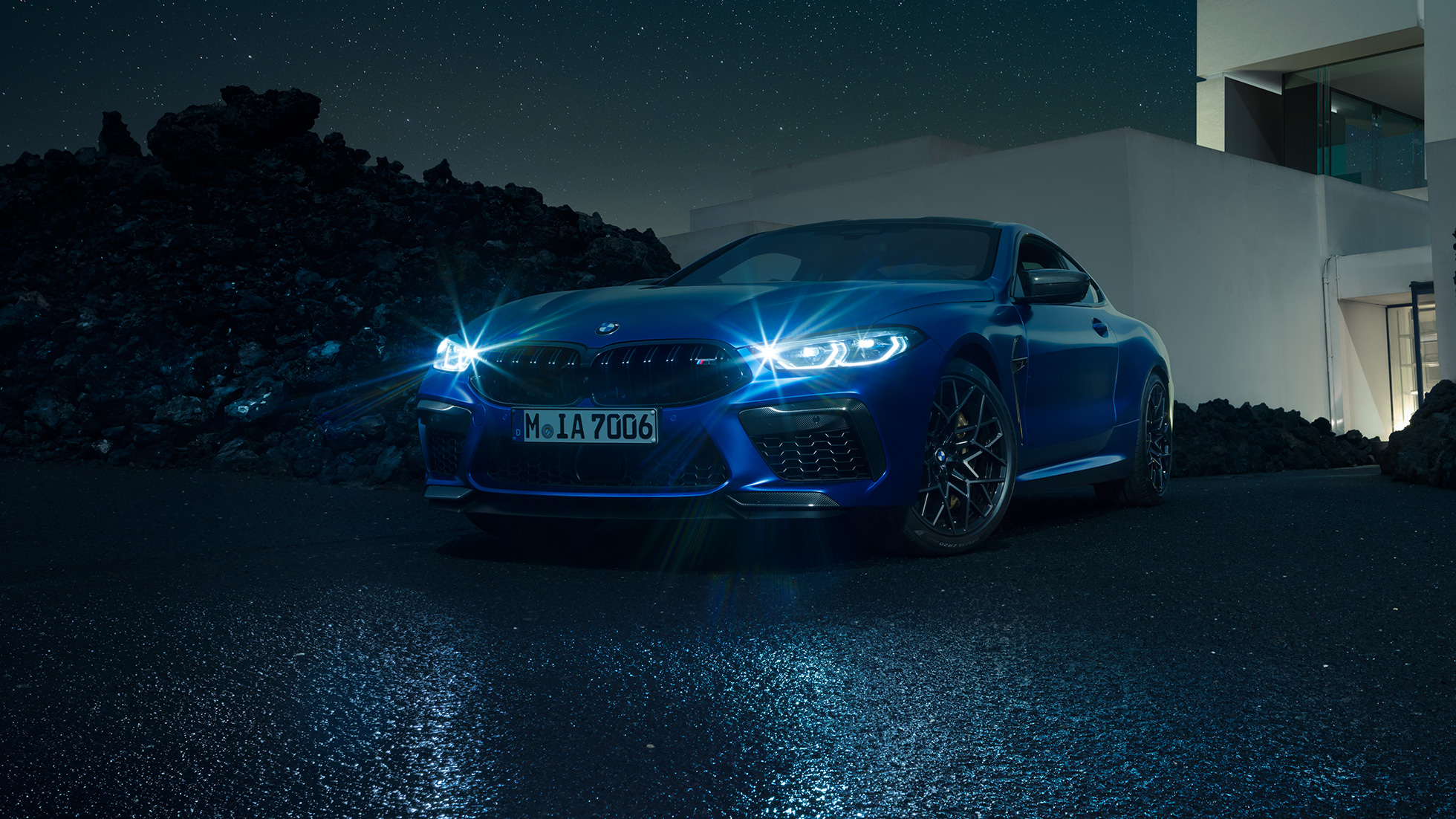 BMW M8 Competition Coupé, Dreiviertel-Frontansicht. F92 BMW M8 Competition Coupé in Marina Bay Blau metallic mit strahlenden LED-Scheinwerfern, stehende Dreiviertel-Frontansicht vor Villa bei Nacht. F92