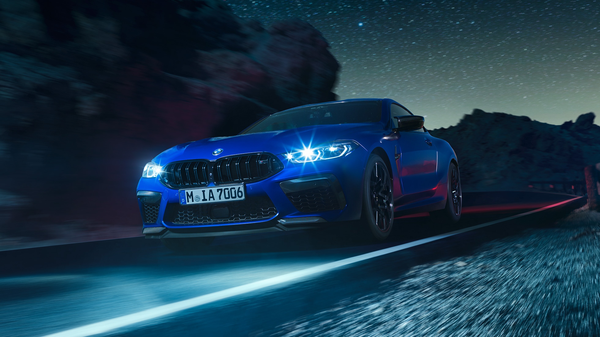 Fahrendes BMW M8 Competition Coupé, Dreiviertel-Frontansicht. F92 BMW M8 Competition Coupé in Marina Bay Blau metallic mit strahlenden LED-Scheinwerfern, Dreiviertel-Frontansicht, fahrend bei Nacht. F92