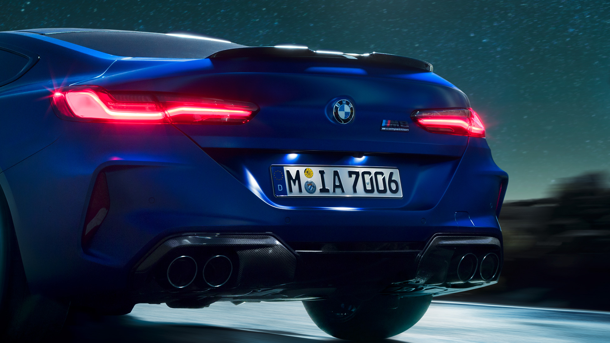 M Diffusor in Carbon Schwarz. F92 BMW M8 Competition Coupé in Marina Bay Blau metallic, Nahaufnahme Heck bei Nacht mit M Diffusor in Carbon Schwarz. F92