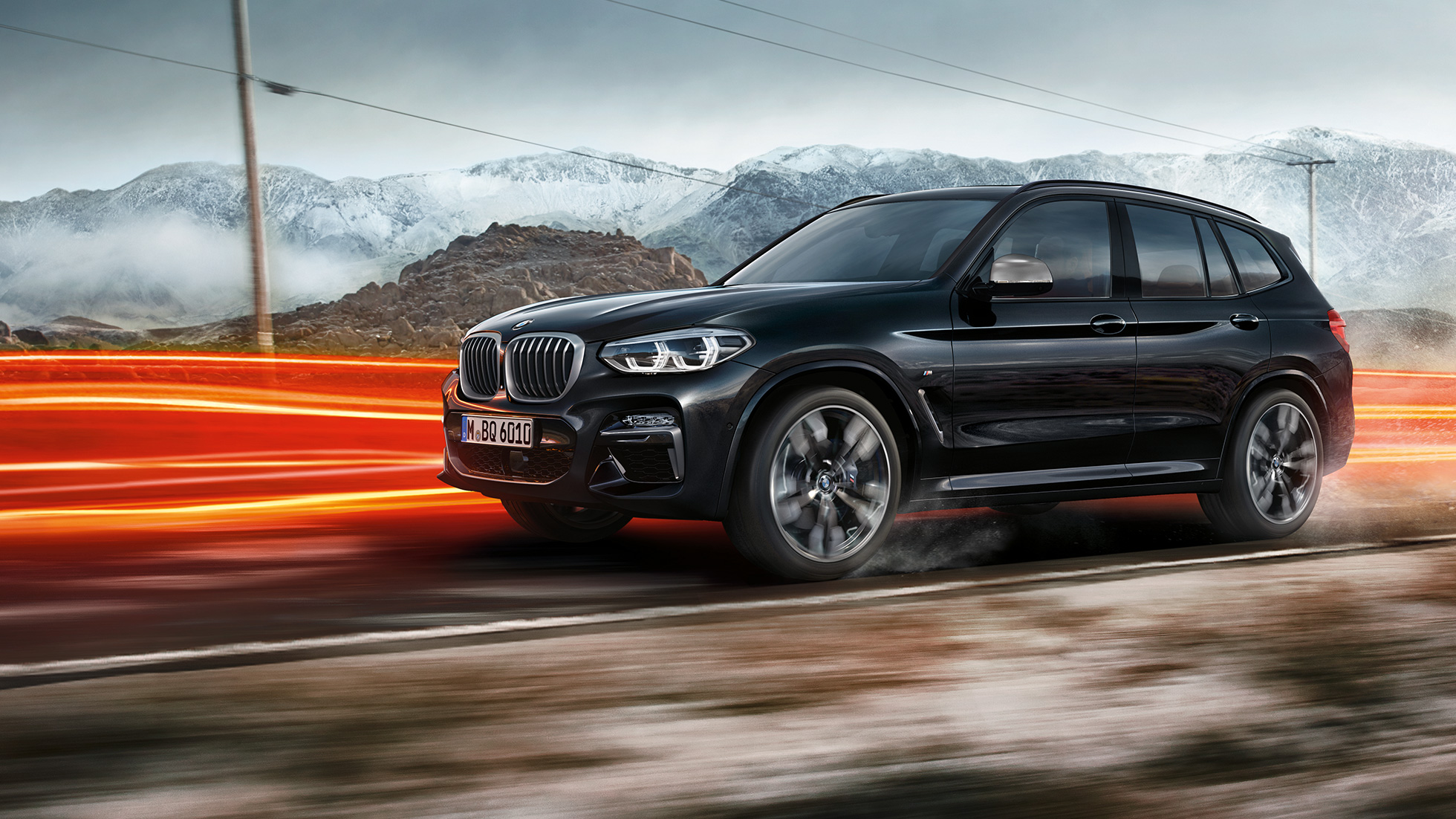 BMW X3 M40i et BMW X3 M40d, vue de profil. Extérieur des BMW X3 M40i et BMW X3 M40d en Saphierschwarz metallic, en mouvement, vue de profil devant un paysage montagneux avec bandes lumineuses.