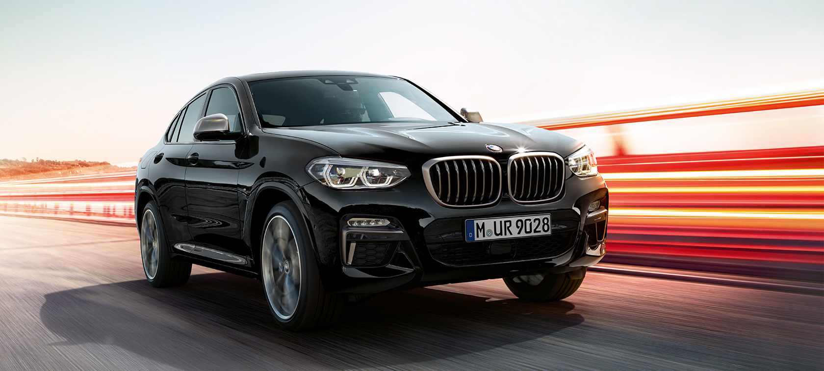 BMW X4 M40i und BMW X4 M40d, Dreiviertel-Frontansicht links. G02 BMW X4 M40i und BMW X4 M40d in Saphierschwarz metallic, fahrend, Exterieur, Dreiviertel-Frontansicht links mit Lichtstreifen. G02