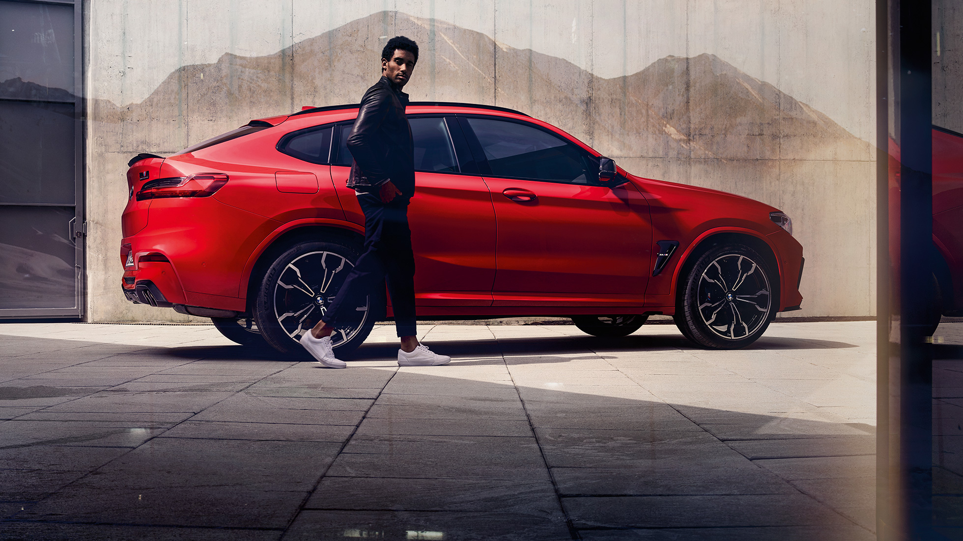 BMW X4 M Competition, Seitenansicht mit jungem Mann. BMW X4 M Competition in Toronto Rot metallic, Exterieur, Seitenansicht mit jungem Mann.