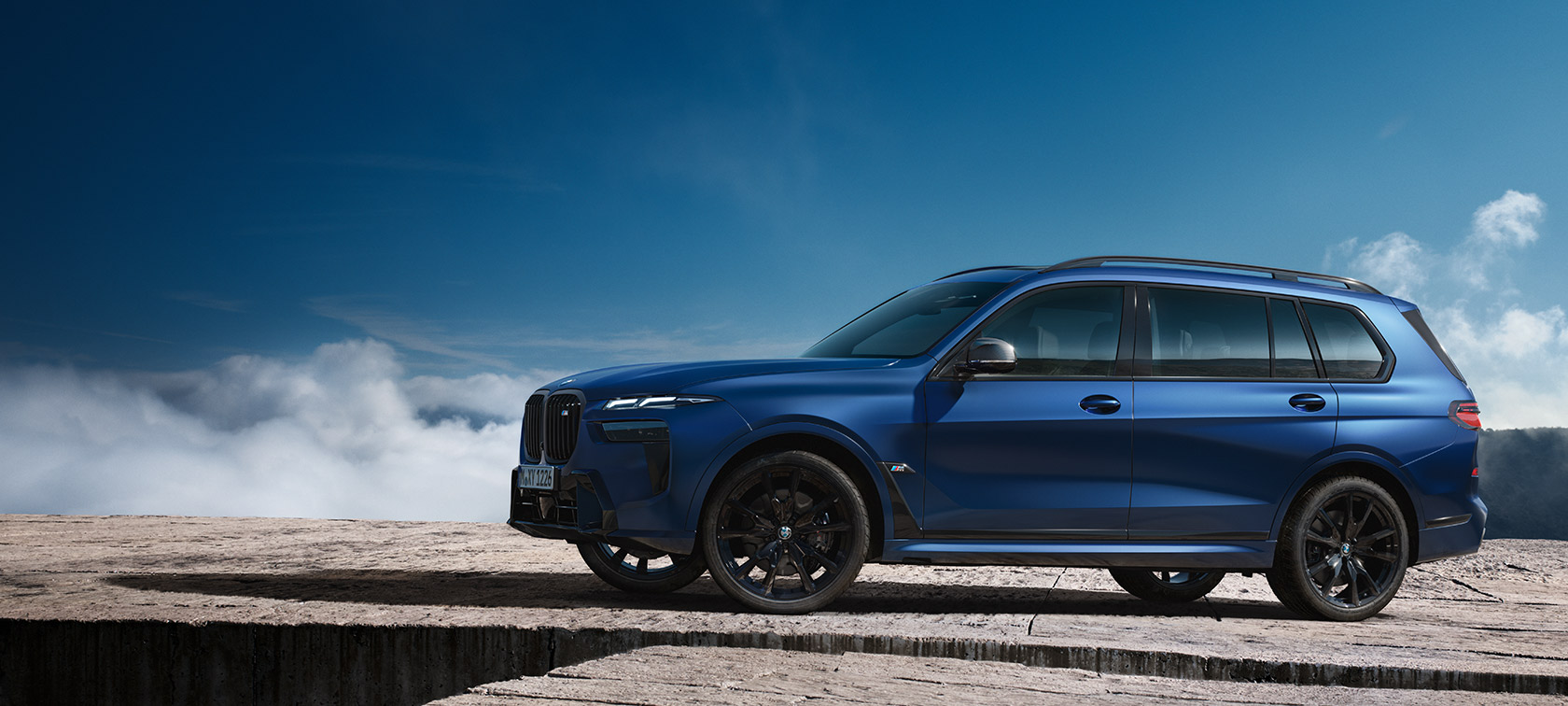 BMW X7 M60i xDrive G07 LCI Frozen Marina Bay Blue – vue de côté devant un paysage de montagne