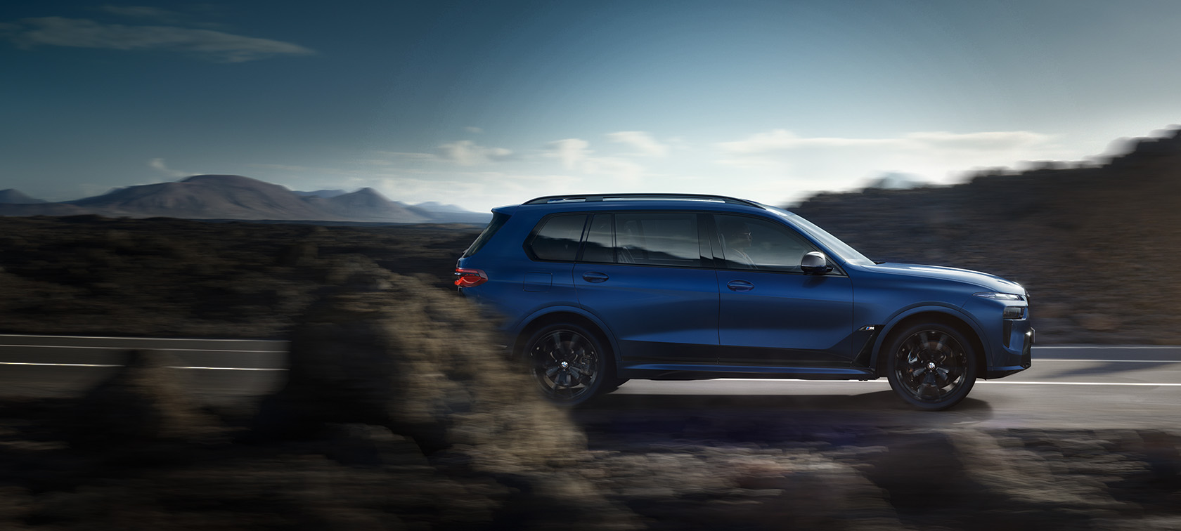 BMW X7 M60i xDrive G07 LCI Frozen Marina Bay Blue – vue de côté sur une route de montagne BMW X7 M60i xDrive G07 LCI Frozen Marina Bay Blue sur la route – vue de côté