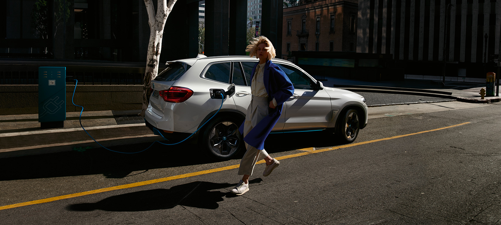 BMW iX3 SUV électrique G08 à une borne de recharge publique, vue de profil BMW iX3 SUV électrique G08 2020 en Mineralweiß metallic à une borne de recharge, vue de profil