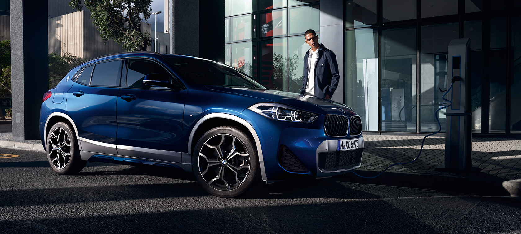 BMW X2 xDrive25e F39 hybride rechargeable, vue de trois quarts de profil branchée à une borne BMW X2 xDrive25e F39 hybride rechargeable, vue de trois quarts de profil branchée à une borne avec modèle