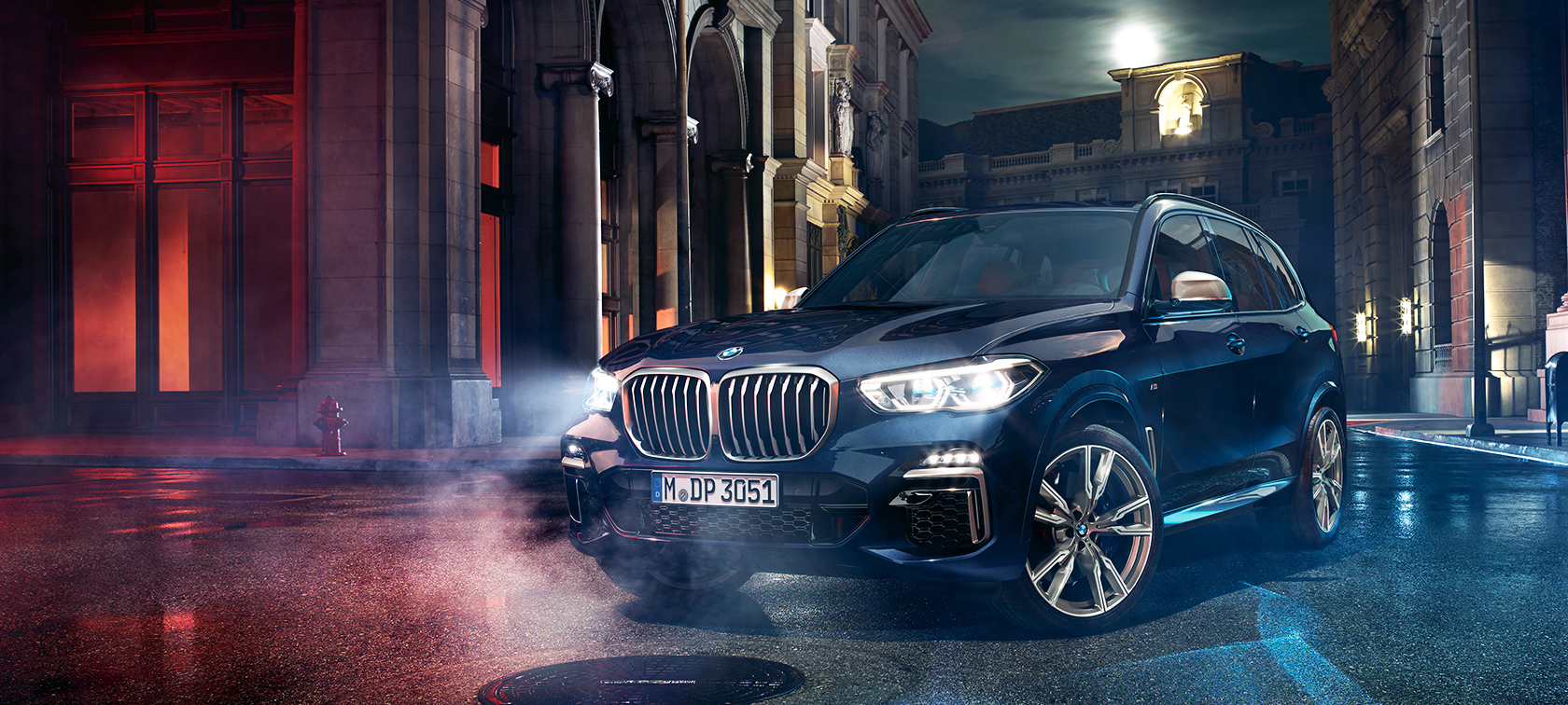 BMW X5 M50d auf der Straße Der BMW X5 M50d steht auf der Straße vor nächtlicher Großstadtkulisse