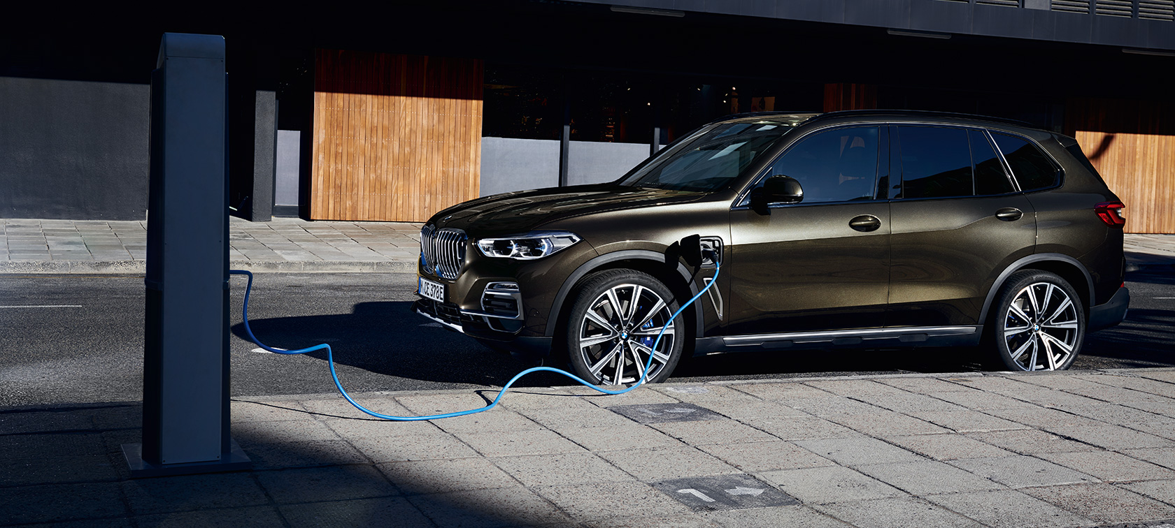 BMW X5 xDrive45e G05 hybride rechargeable, vue de trois quarts de profil BMW X5 xDrive45e G05 hybride rechargeable, branchée à une borne de recharge, vue de trois quarts de profil