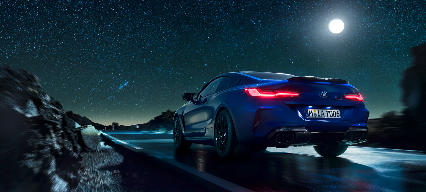 BMW M8 Competition Coupé, vue arrière. BMW M8 Competition Coupé en marche, vue arrière de nuit sous la pleine lune.