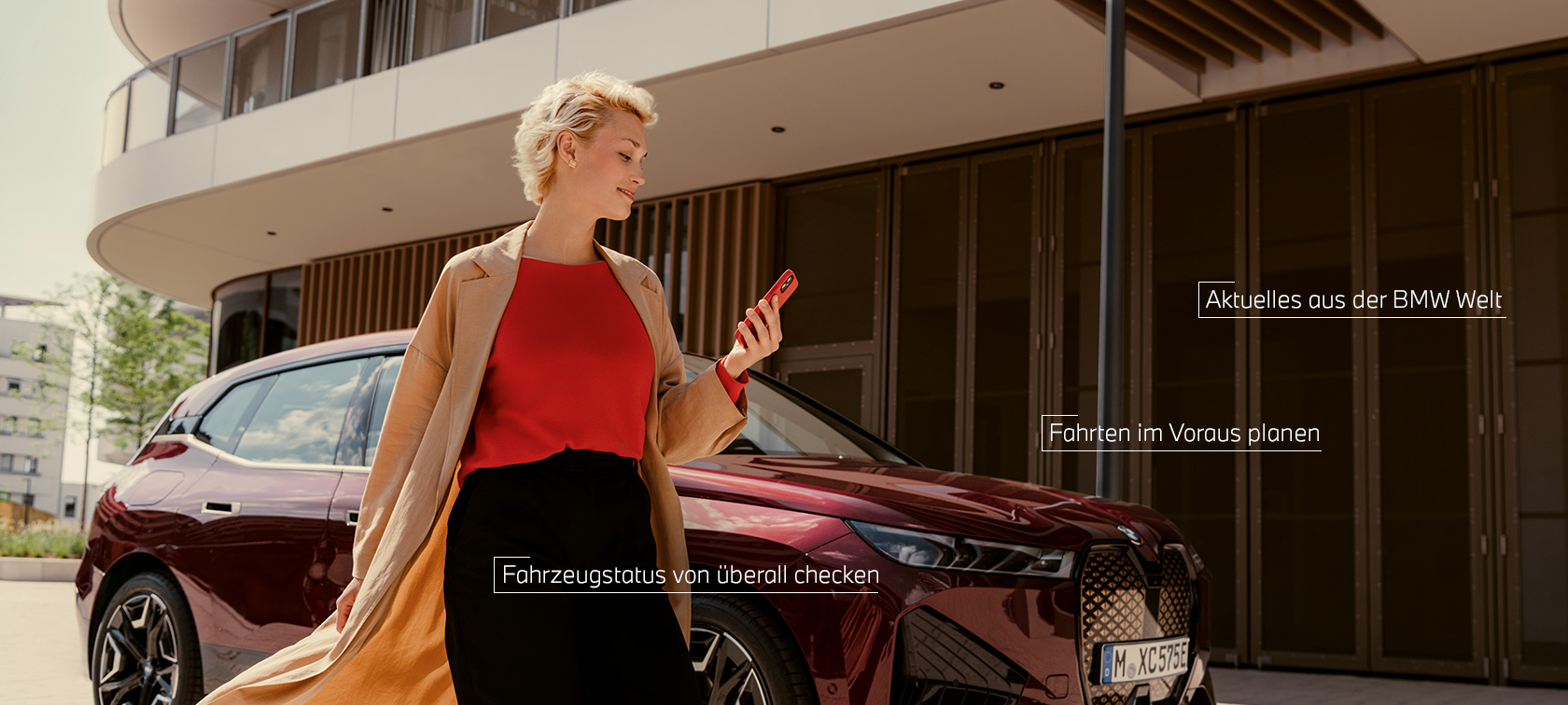 Frau vor BWW iX und benutzt My BMW App auf Smartphone Frau vor BWW iX und benutzt My BMW App auf Smartphone