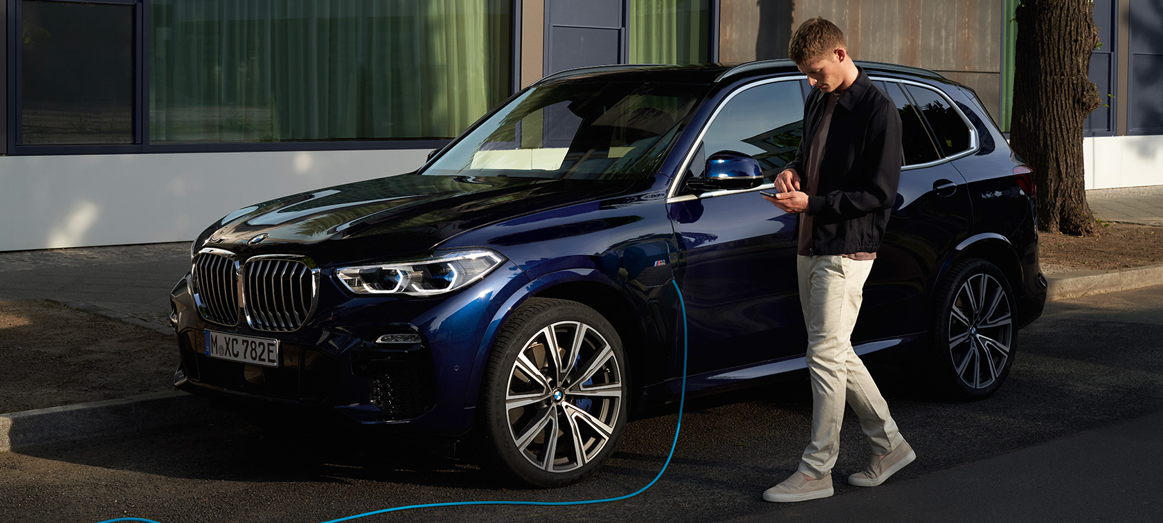 Un homme utilise My BMW App sur son smartphone. Un homme utilise My BMW App de BMW ConnectedDrive sur son smartphone pendant que sa BMW X5 Plug-in Hybrid est en train de charger