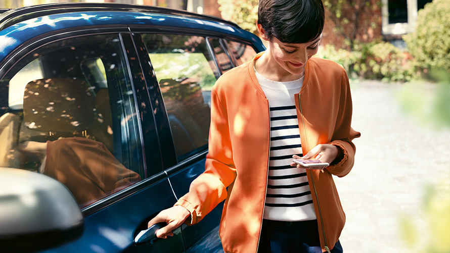 BMW Teleservices Frau mit Smartphone in der Hand vor ihrem BMW