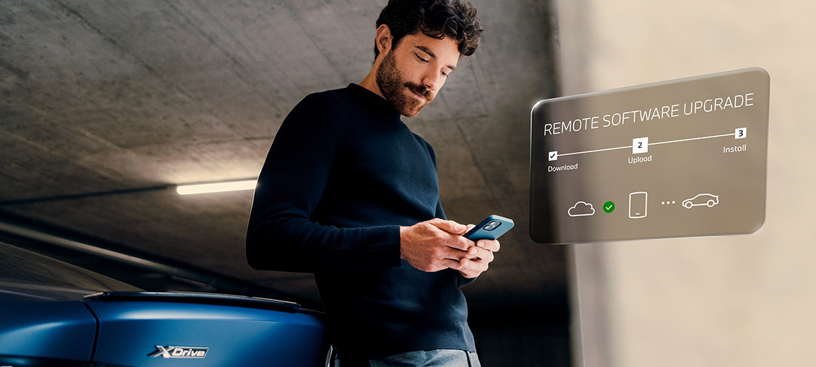 Homme adossé à l’arrière d’une BMW et regardant son smartphone Remote Software Upgrade, homme adossé à l’arrière d’une BMW et regardant son smartphone