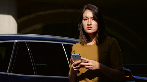 Services numériques BMW ConnectedDrive Aperçu femme avec smartphone devant BMW