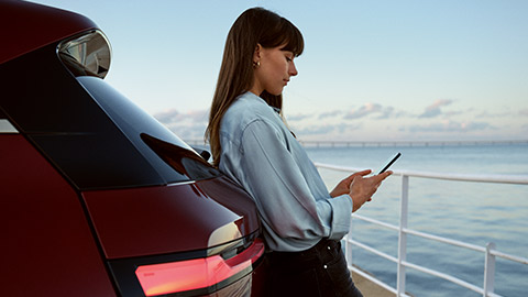 Une femme utilise My BMW App de BMW ConnectedDrive sur son smartphone, devant une BMW X5 blanche.