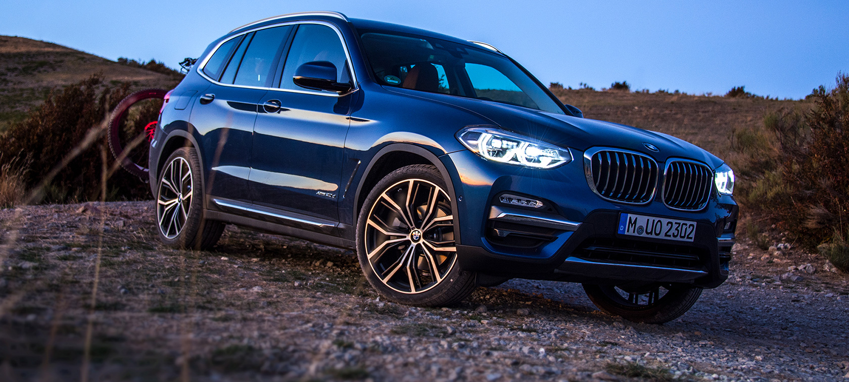 Dunkelblauer BMW X3 im Gelände Dunkelblauer BMW X3 im Stand mit Heckträger und Mountainbike im Gelände