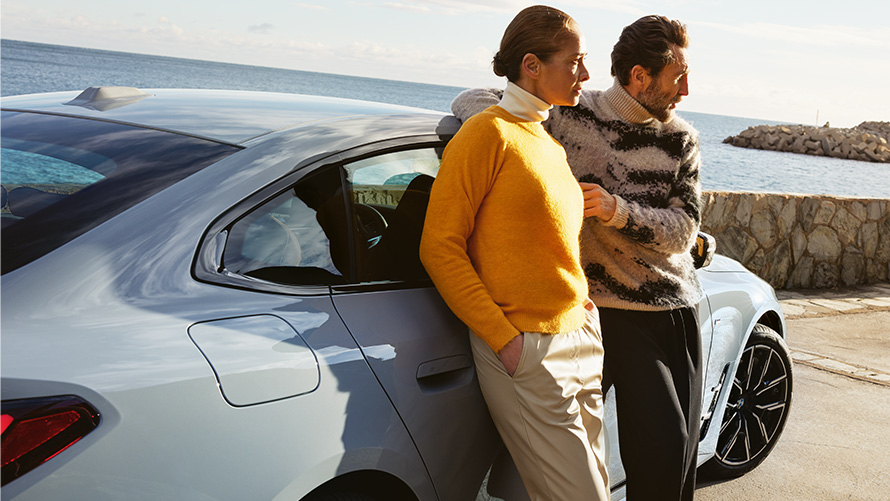BMW Service Inclusive Dauer und Laufzeiten für Neuwagen BMW Service Inclusive Mann und Frau lehnen an BMW i4 vor Küste