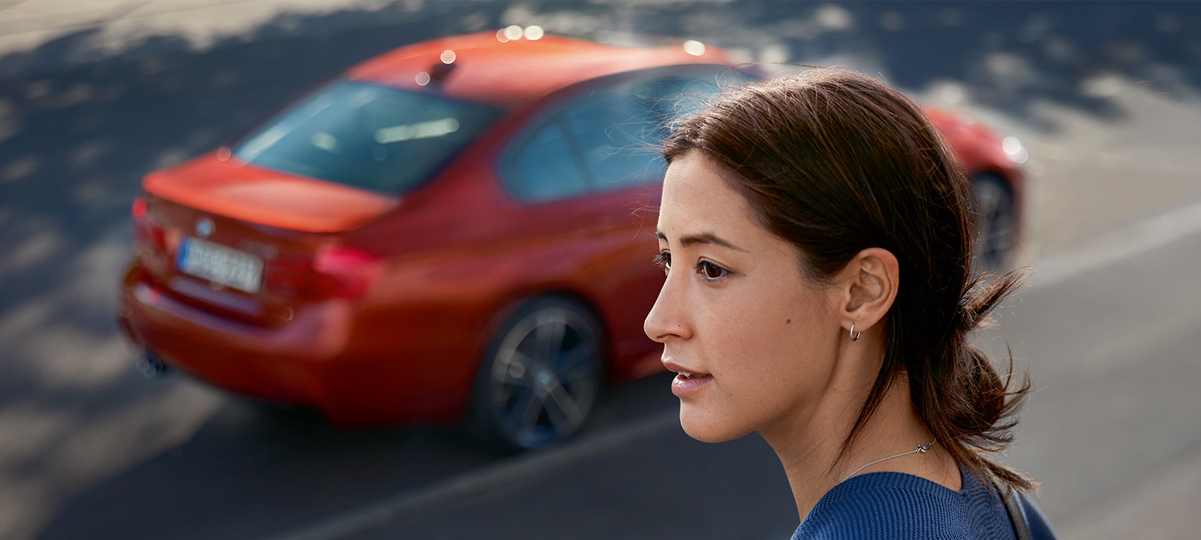 Hier bitte Text ergänzen in EN A woman looking into the distance. A BMW passes behind her.